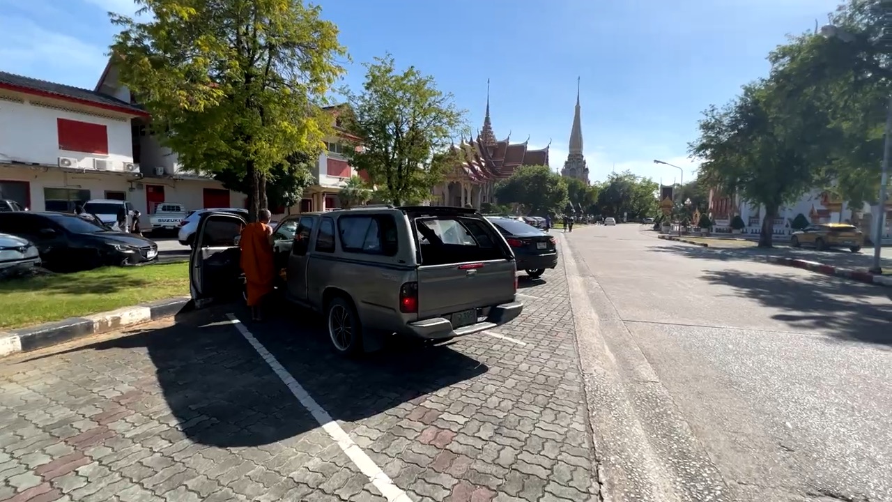 Un moine en robe orange descend d'un pick-up sur le parking du temple