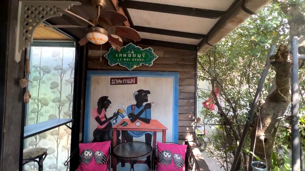 La terrasse en bois du café Le Noi Berry, coussins roses et fresque murale